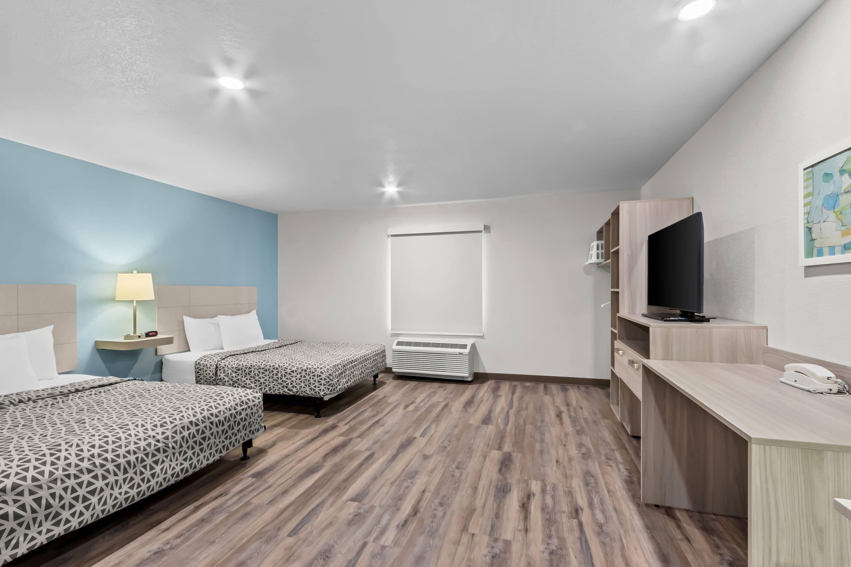 A hotel room with two beds, a desk, a TV, and a window.