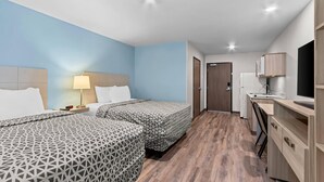 Habitación de hotel con dos camas, un escritorio, una silla, un televisor y una kitchenette.