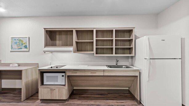 Una cocina moderna con armarios de madera, microondas integrado, un lavabo y un refrigerador blanco.