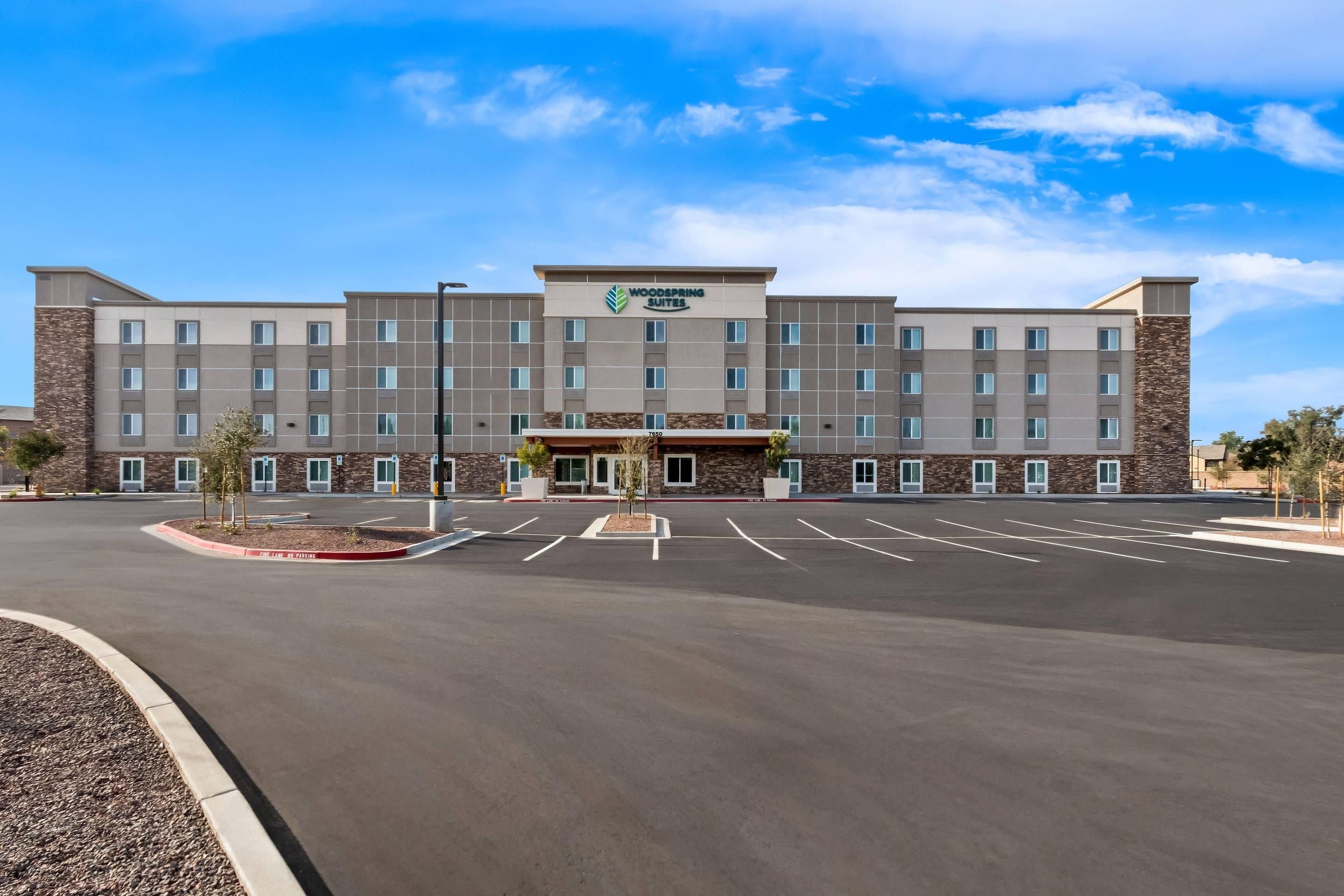 A multi-story hotel with a flat roof, a central entrance, and a parking lot in front.