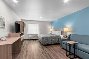 Habitació d'hotel amb llit, escriptori amb telèfon, televisió, sofà i tauleta de nit amb làmpades.