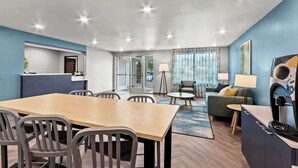 A modern hotel room with a wooden dining table, chairs, a sofa, a small round table, and a coffee machine. - Woodspring Suites Gilbert - Mesa Gateway Airport (Gilbert)