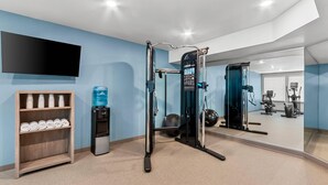 Un gimnasio con equipamiento de ejercicio, un dispensador de agua y un televisor instalado en la pared.