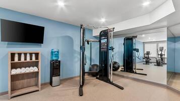 A gym with exercise equipment, a water dispenser, and a TV mounted on the wall.
