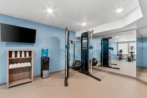 Un gimnasio con equipo de ejercicio, un dispensador de agua y un televisor montado en la pared.