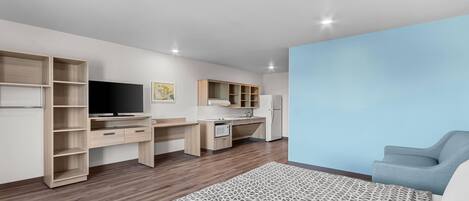 Un dormitorio moderno con cama, escritorio, televisor y kitchenette.