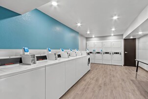 Un lavadero comercial con varias lavadoras y secadoras, una pared de acento azul y suelo de madera.