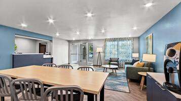 A modern hotel room with a dining area, a sofa, and a TV.