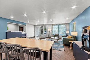 Habitación de hotel moderna con zona de comedor, sofá y televisor.