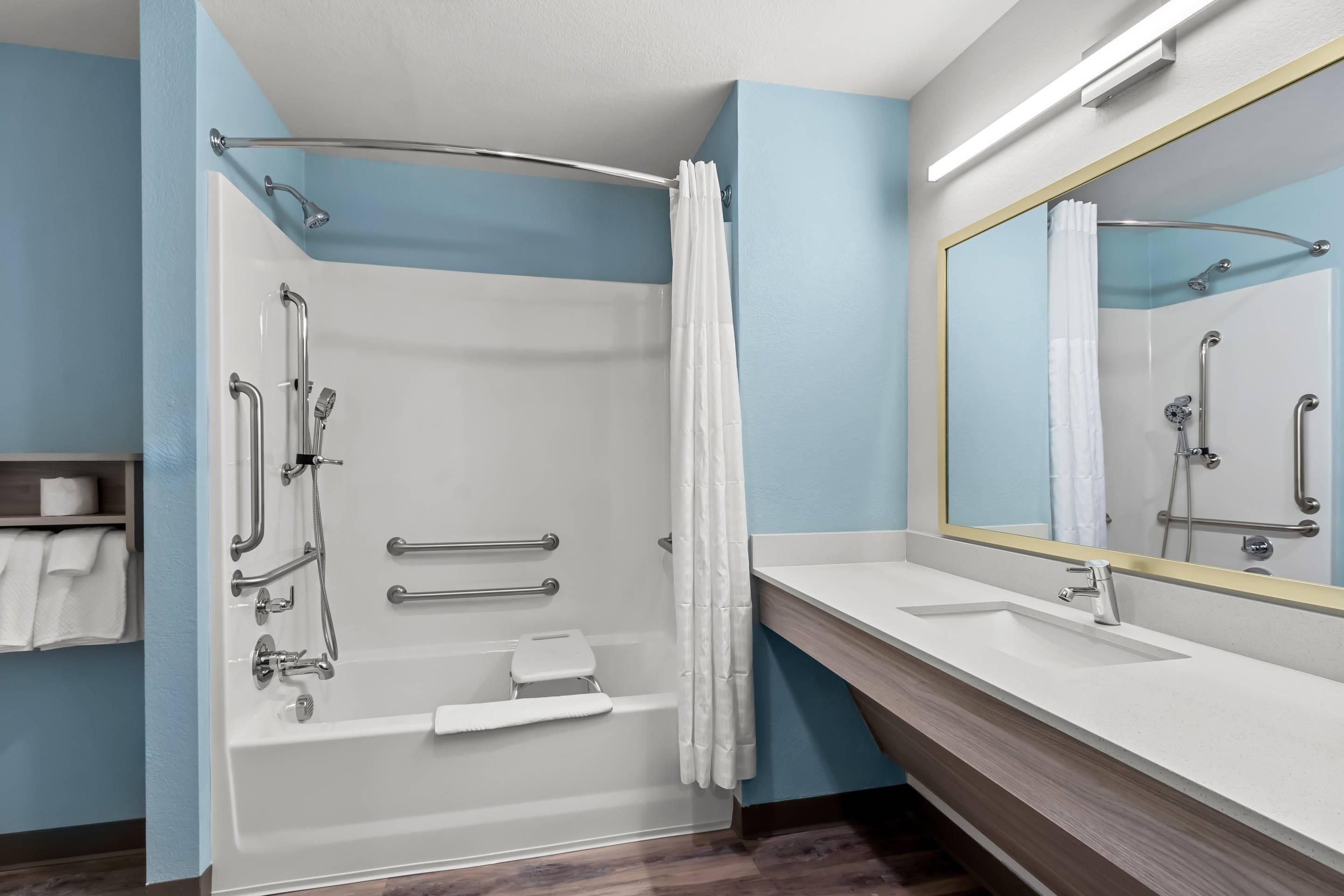 A modern bathroom with a walk-in shower, grab bars, a white bathtub, and a large mirror.