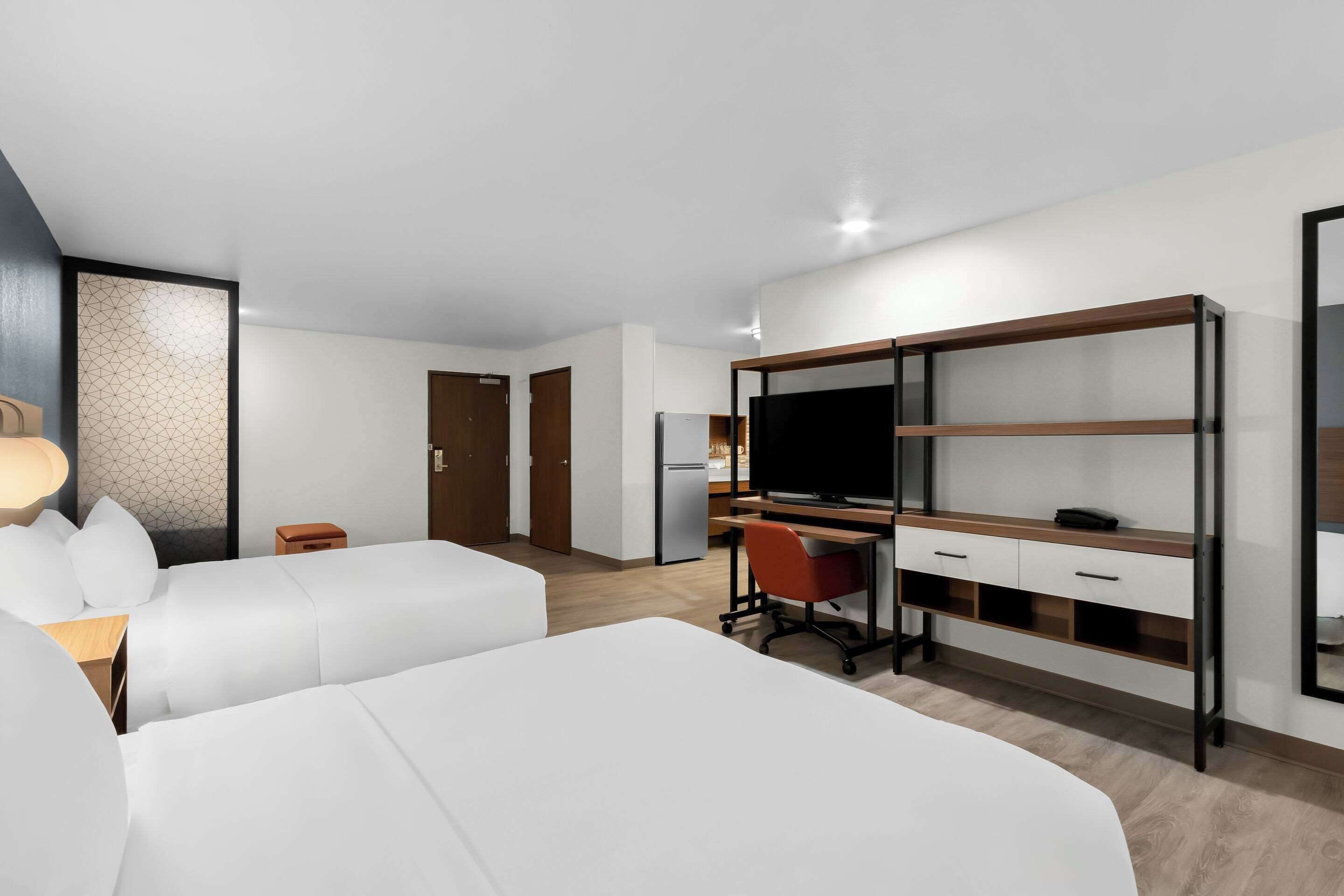 Une chambre d’hôtel moderne avec deux lits blancs, un bureau avec un ordinateur, une télévision et une armoire.