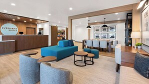 A modern hotel lobby with a reception desk, seating area with sofas and chairs, and a dining area with tables and chairs.