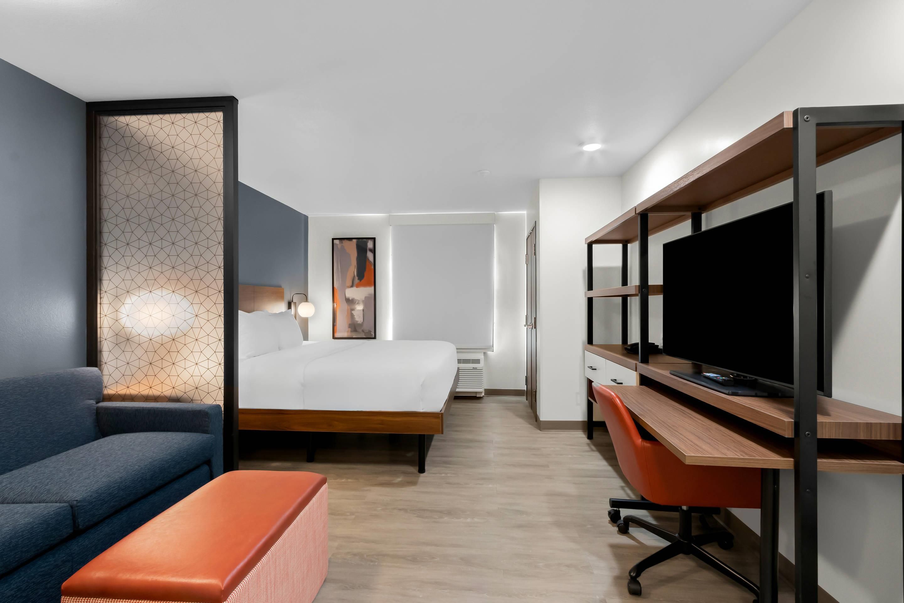 Quarto de hotel moderno com cama, escrivaninha, televisão e sofá.