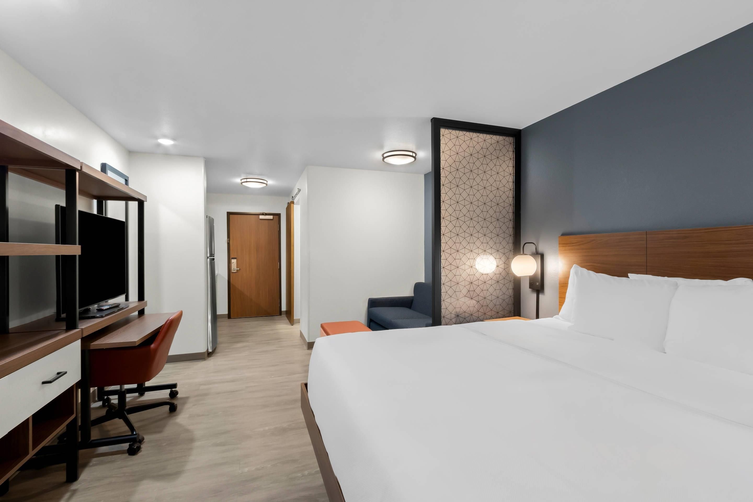 A hotel room with a bed, a desk with a computer, a television, and a seating area.