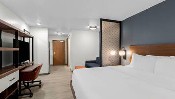 A hotel room with a bed, a desk with a computer, a television, and a seating area.