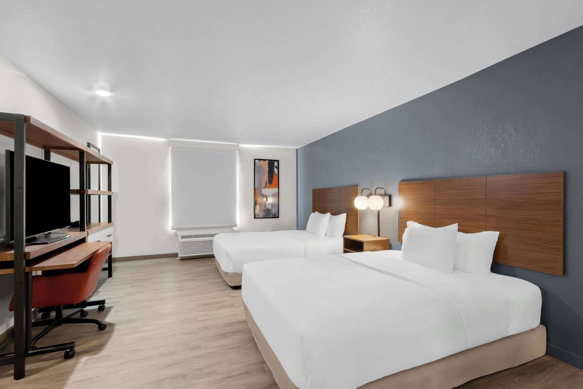 Habitación de hotel con dos camas, un escritorio con computadora, una silla y un televisor.