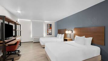 A hotel room with two beds, a desk with a computer, a chair, and a TV.
