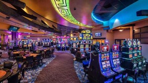 A casino with multiple slot machines, tables, and chairs.