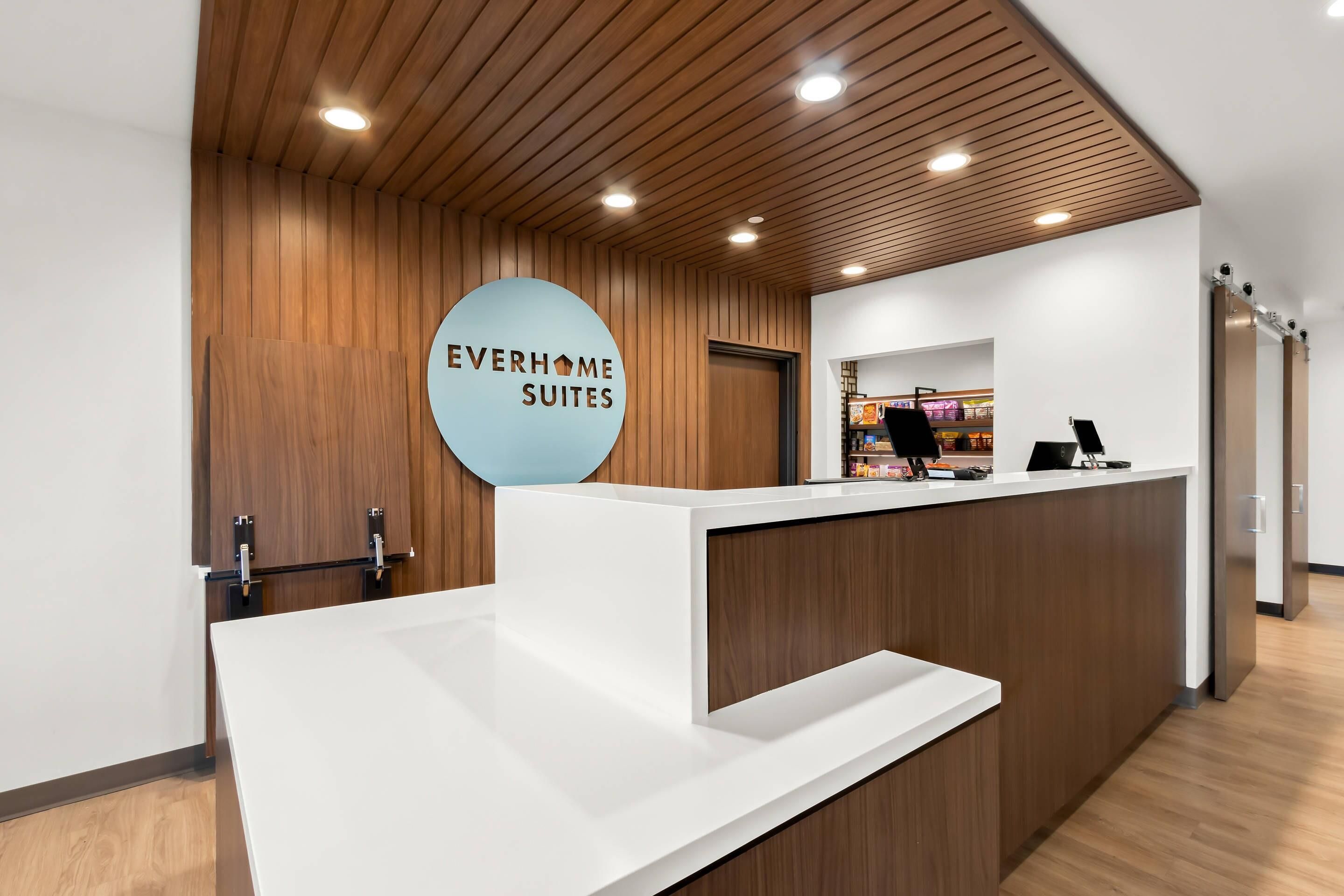 En receptionsdisk med skiltet 'EVERHOME SUITES' i en moderne hotellobby med træpaneler og indbygget belysning.