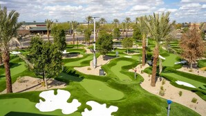 A golf course with sand bunkers, palm trees, and a clear sky.