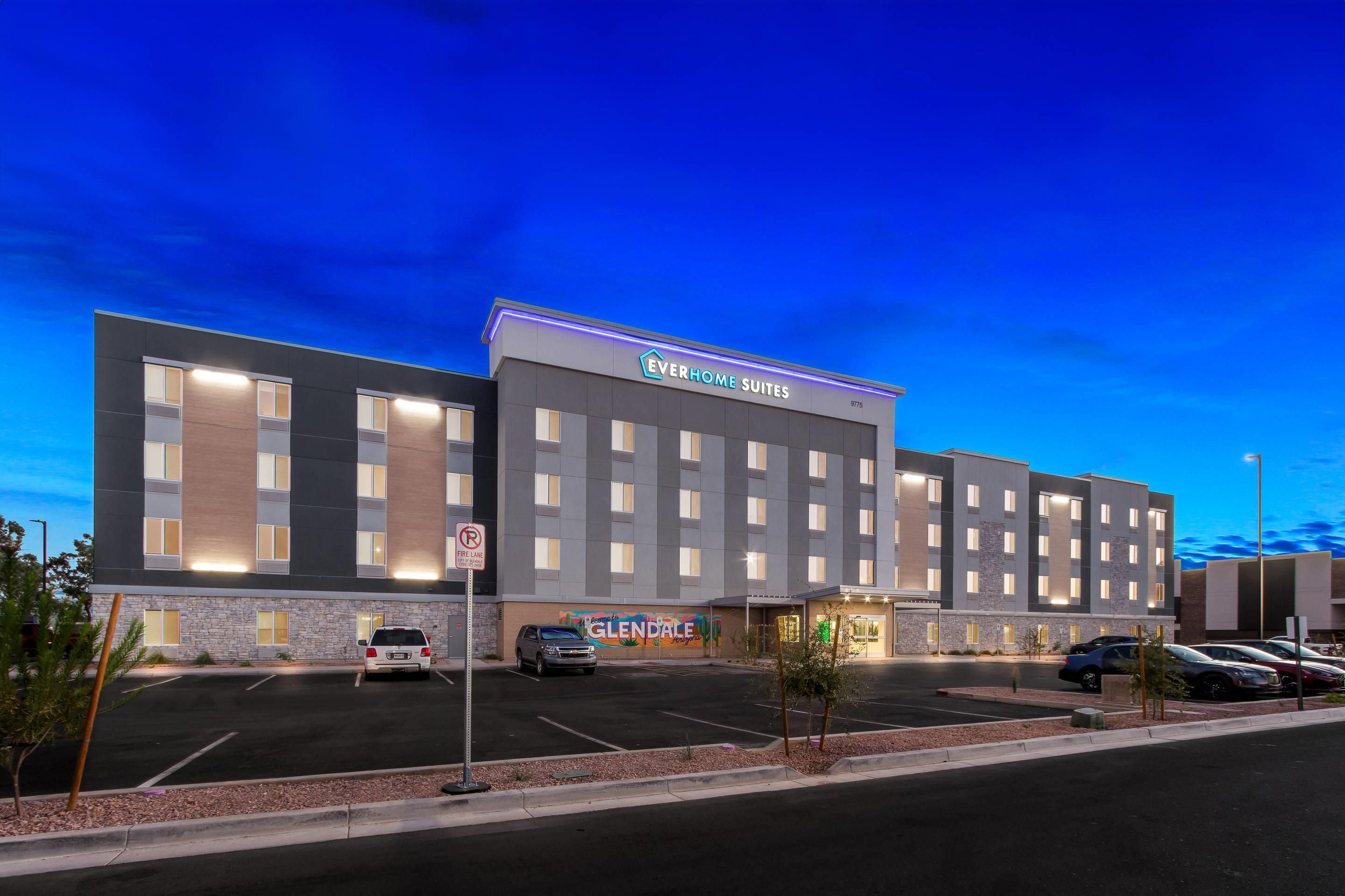 A multi-story hotel with a flat roof, a parking lot in front, and a sign for 'EVERHOME SUITES'.