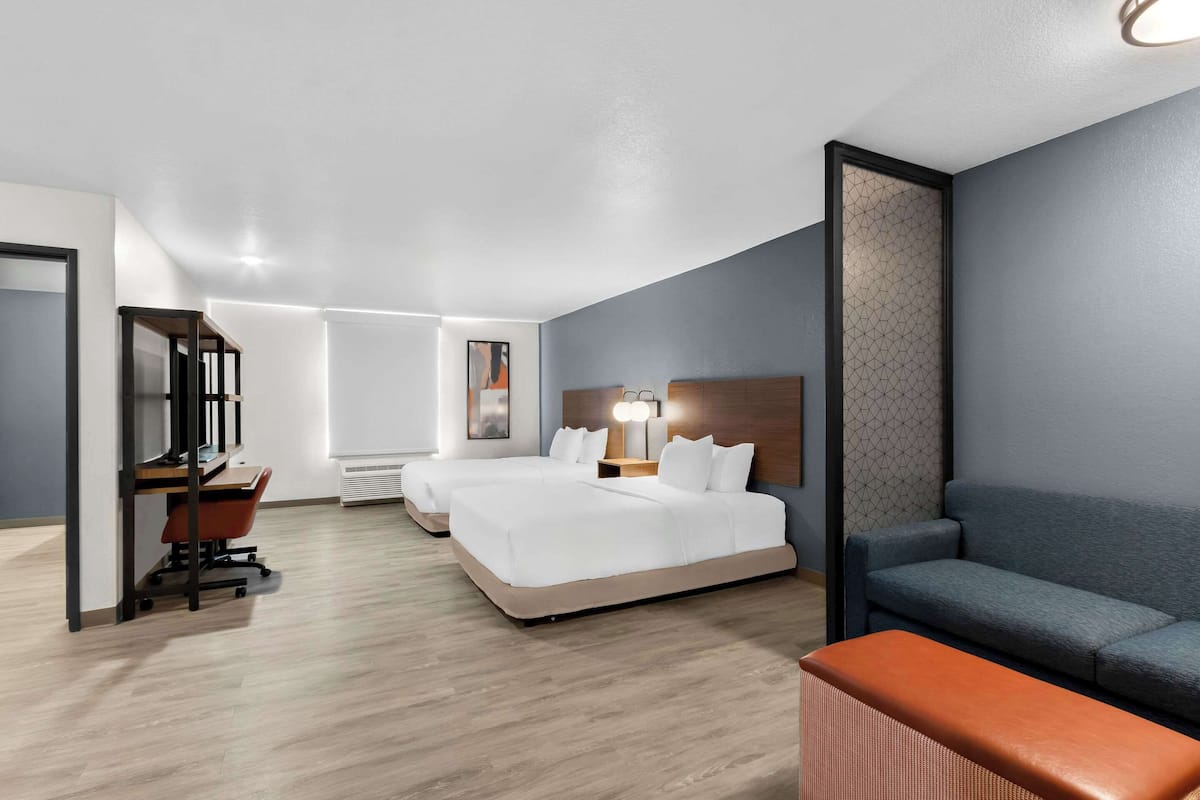 Una habitación de hotel moderna con escritorio, dos camas, un sofá y un amplio ventanal.