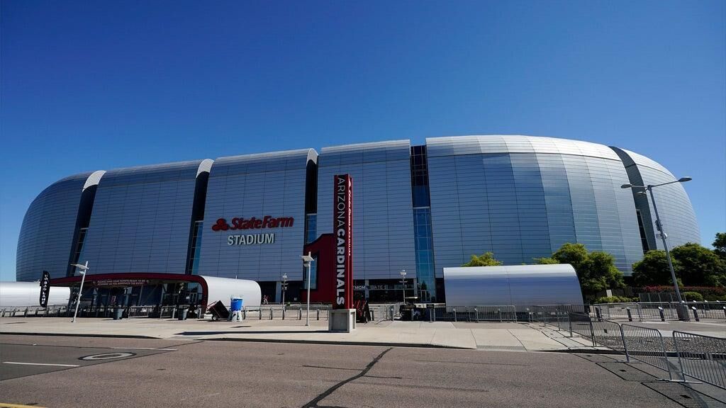 A large stadium with a curved facade, a prominent red sign, and a clear blue sky.