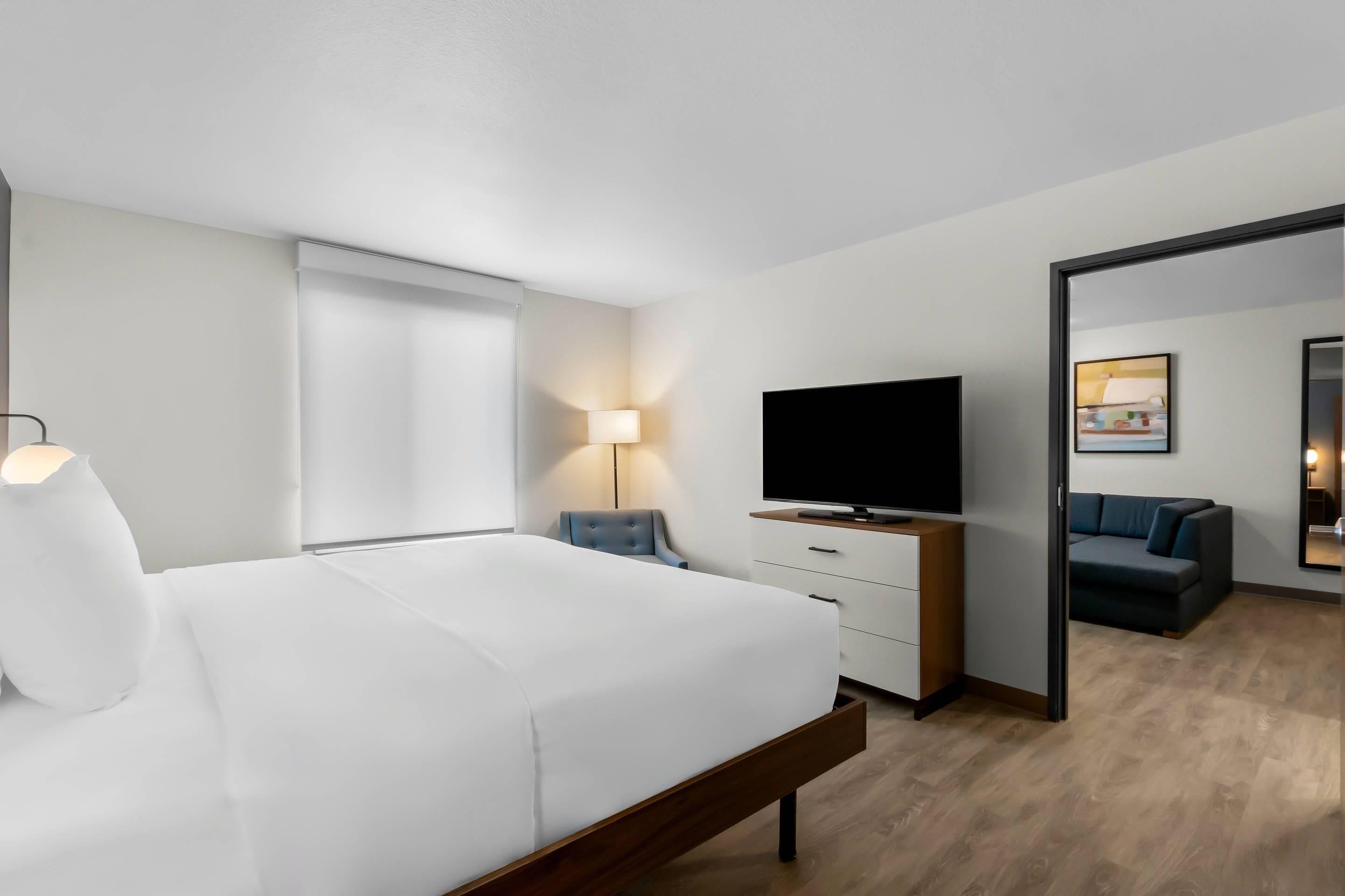 Habitación de hotel con cama, televisión, escritorio, silla, lámpara y espejo.