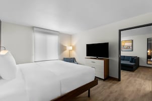 Habitación de hotel con cama, televisión, escritorio, silla, lámpara y espejo.