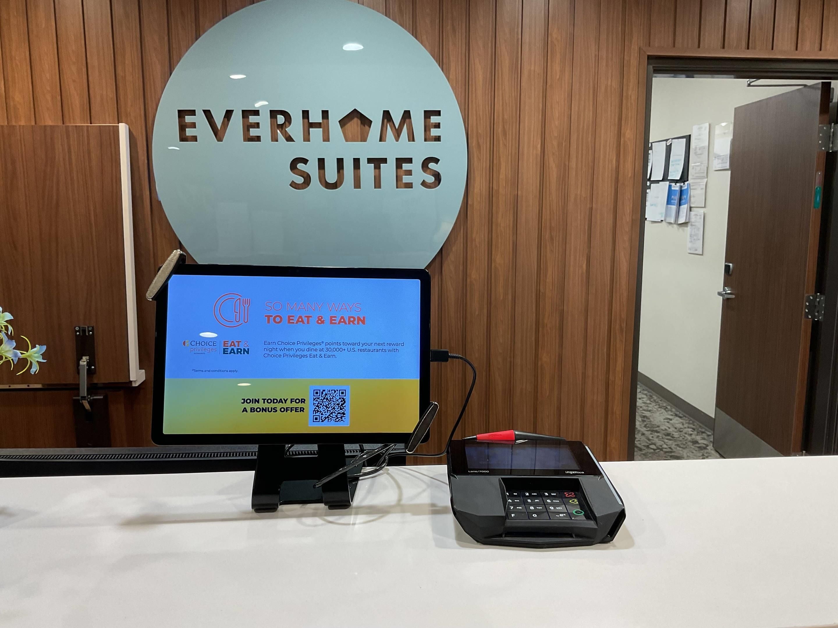 Ein Empfangsschalter mit einem Monitor, der eine Werbeanzeige für ein Treueprogramm, einen QR-Code und ein Zahlungsterminal zeigt.