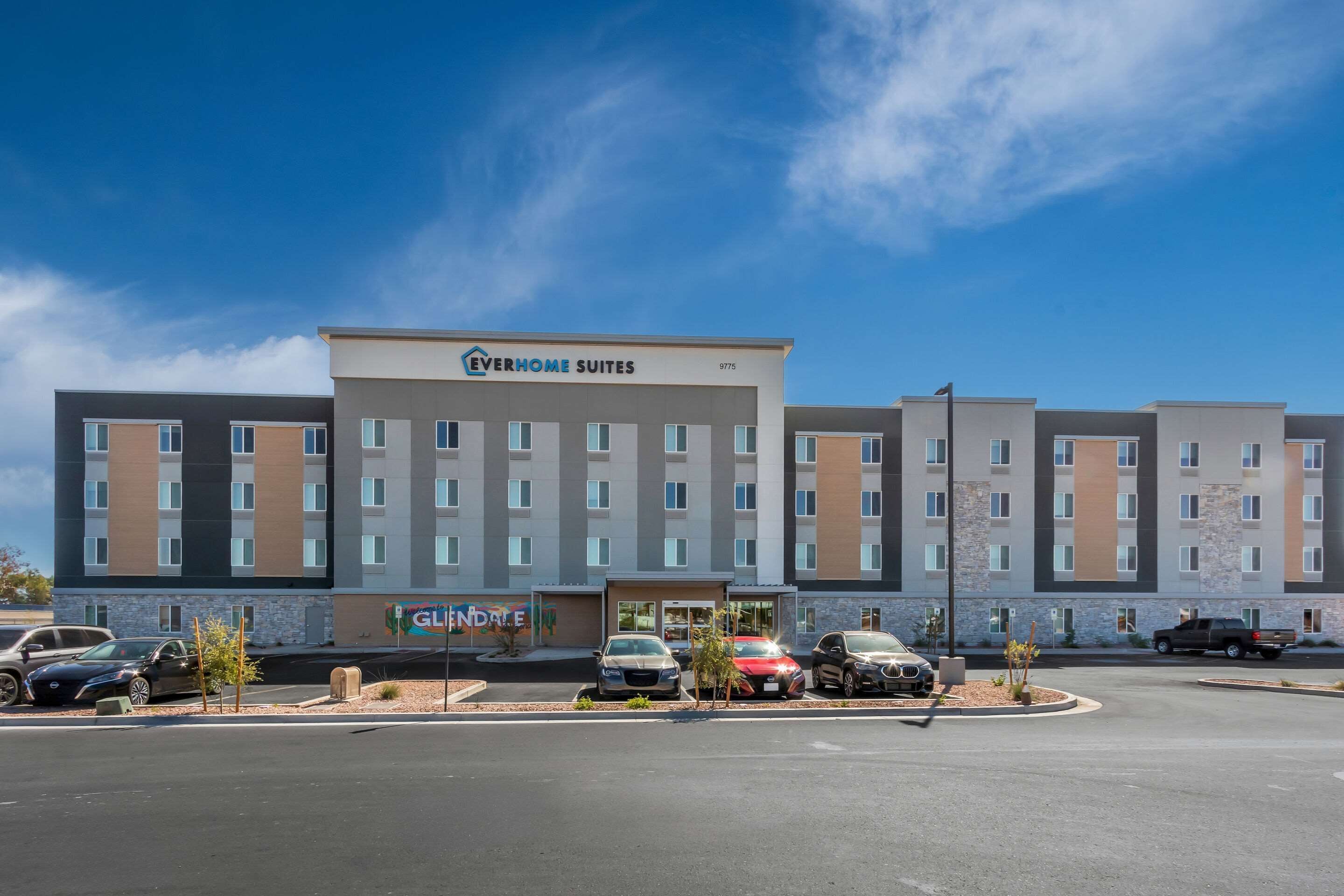 Et hotel med flere etager, en central indgang og en parkeringsplads med flere biler.