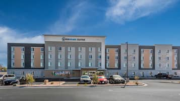 Et hotel med flere etager, en central indgang og en parkeringsplads med flere biler.