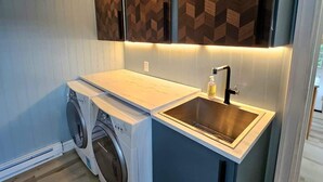 Une petite buanderie équipée d’un lave-linge, d’un évier et d’un panneau mural en bois.