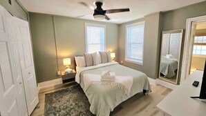 Une chambre à coucher avec un lit, des tables de chevet, un ventilateur de plafond et un grand miroir.