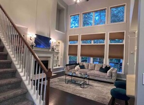 A spacious living room with a staircase, a large window with multiple panes, a comfortable sofa, and a flat-screen TV.