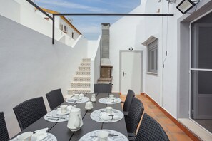 A dining area with a table set for six, surrounded by wicker chairs, white walls, and a tiled floor.
