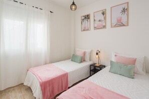 A bedroom with two beds, a nightstand, a lamp, and three framed pictures on the wall.