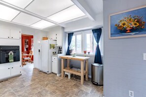 Une cuisine de taille réduite avec des meubles blancs, une table en bois et une fenêtre ornée de rideaux bleus.