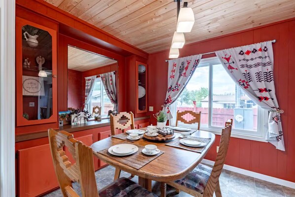 Un coin repas avec une table en bois, des chaises et une fenêtre agrémentée de rideaux à motifs.
