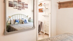 Une chambre avec un grand miroir, un lit avec des oreillers bleus et blancs, une commode et un berceau.