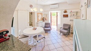 Une cuisine avec une table blanche, deux chaises, un appareil électroménager rouge et une porte donnant sur un balcon.
