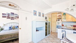 Une pièce comprenant un lit, une armoire bleue, un coin cuisine avec des placards et un réfrigérateur, ainsi qu’une table à manger avec des chaises.
