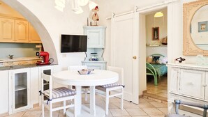 Une cuisine de taille réduite comprenant un coin repas, un téléviseur et une porte donnant sur une autre pièce.