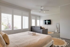 Une chambre à coucher avec un lit, un canapé gris, un ventilateur de plafond, une télévision et un miroir.