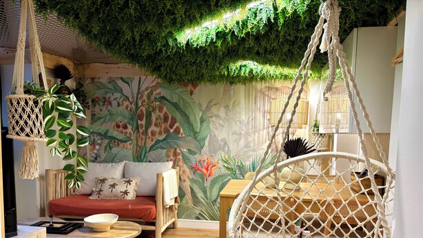 Een gezellige woonkamer met een macrame stoel, een houten bijzettafeltje en een bank met kussens.