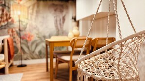 Een macramé stoel, een houten eettafel en stoelen in een kamer met een muurschildering.