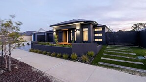 Una casa moderna con techo plano, un porche cubierto y un césped cuidado con piedras para pisar.
