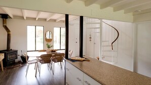 A modern kitchen with a central island, a built-in stove, and a spiral staircase. - Quindy Beach Cottage – Steps to the Bay (Quindalup)