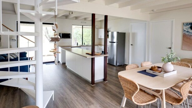 A modern kitchen with a central island, white cabinetry, and stainless steel appliances. - Quindy Beach Cottage – Steps to the Bay (Quindalup)