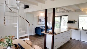 A modern kitchen with white cabinetry, a built-in microwave, and a window overlooking the outdoors. - Quindy Beach Cottage – Steps to the Bay (Quindalup)